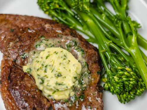 steak topped with herb butter with a side of broccoli stem.