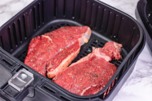 raw steaks in air fryer basket.