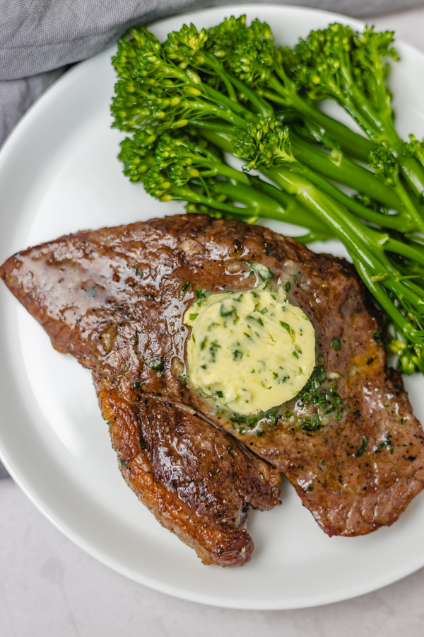 steak topped with garlic butter served with broccolini. 