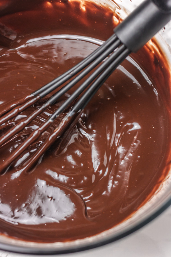 a black whisk in a bowl of melted chocolate.