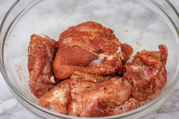 chicken marinating in a glass bowl.