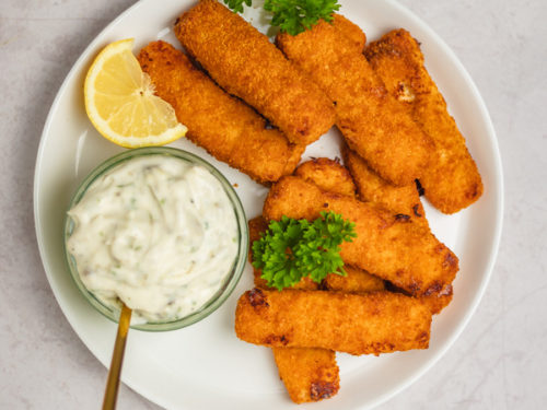 a plate of breaded fish and tartar sauce with a lemon wedge.