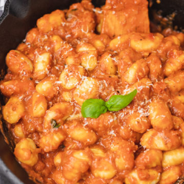 a skillet of gnocchi and tomato sauce garnished with fresh basil leaves.