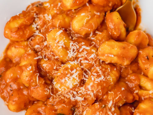 a plate of gnocchi in red sauce topped with parmesan cheese.