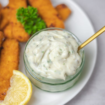 a pot of white sauce with fish sticks and a lemon wedge.