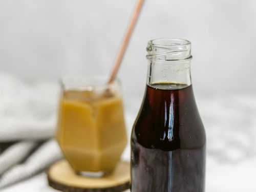 a cup of coffee placed beside a bottle containing brown liquid.