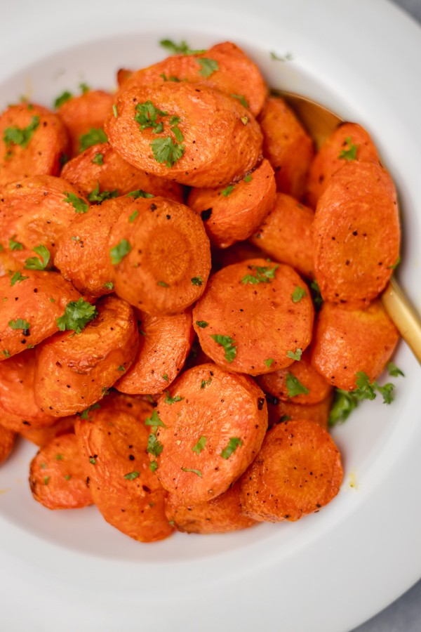 a close view of roasted chopped carrots garnished with chopped parsley on a white plate.