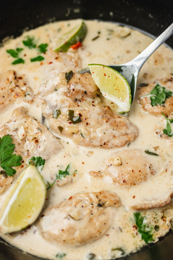 a close up on chicken thighs in creamy sauce with lime wedges.