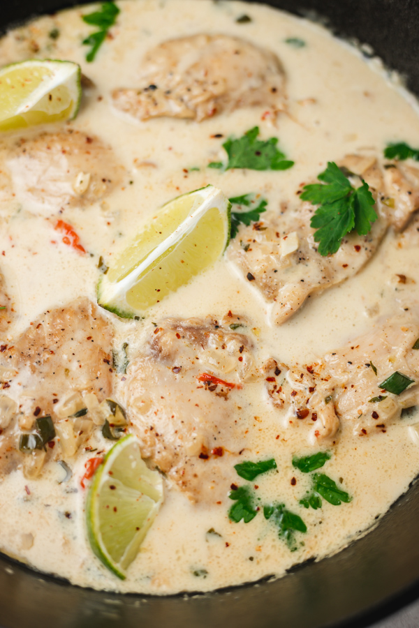 a skillet of chicken thighs in creamy sauce garnished with three lime wedges.