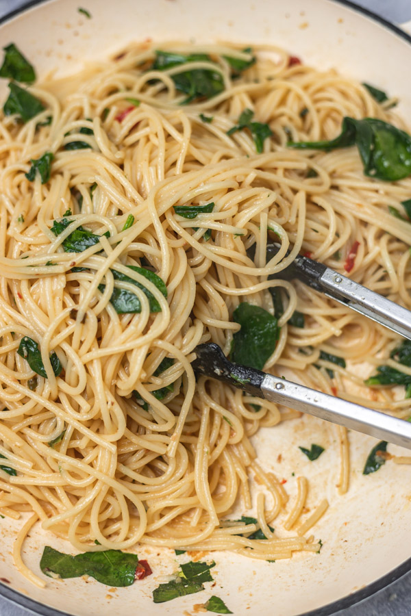 a pan of garlic butter spaghetti with spinach and a black tong.