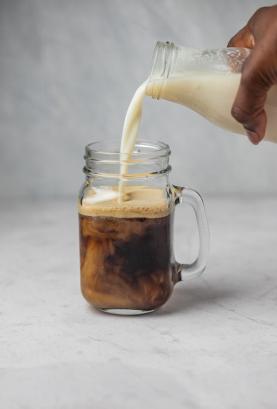 a hand pouring milk into a glass of coffee.