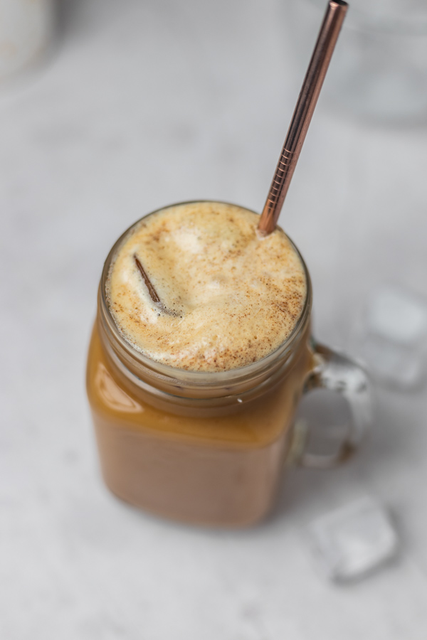 A glass of iced coffee with a frothy top.