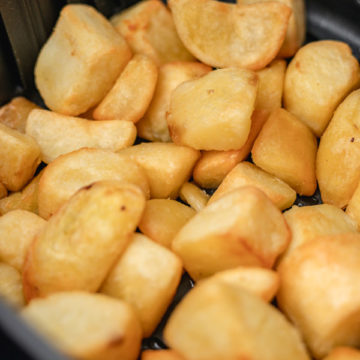 golden and crispy roast potatoes in the air fryer basket.