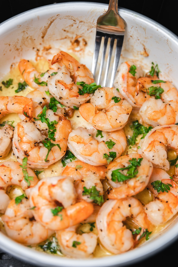 juicy and plump shrimp garnished with chopped parsley in a white enamel baking dish.