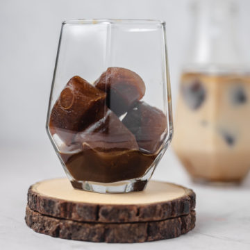 a glass of frozen coffee cubes placed on two wooden coaster.