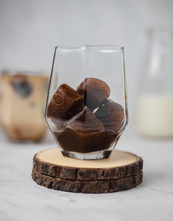 a glass filled with frozen coffee cubes place on 2 wooden coaster.