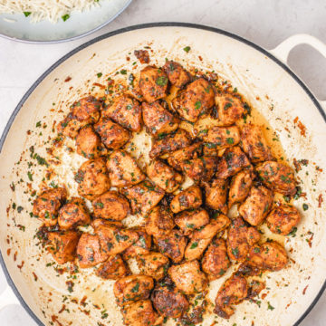 an overhead shoot of cooked chicken bites in a skillet placed beside a bowl of white rice.