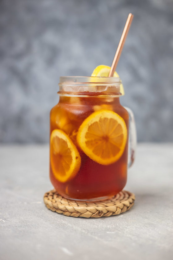 a glass of iced tea with straw placed on a woven coaster.