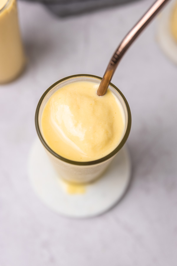 a close top view of creamy and thick mango pineapple smoothie in a glass with a straw.