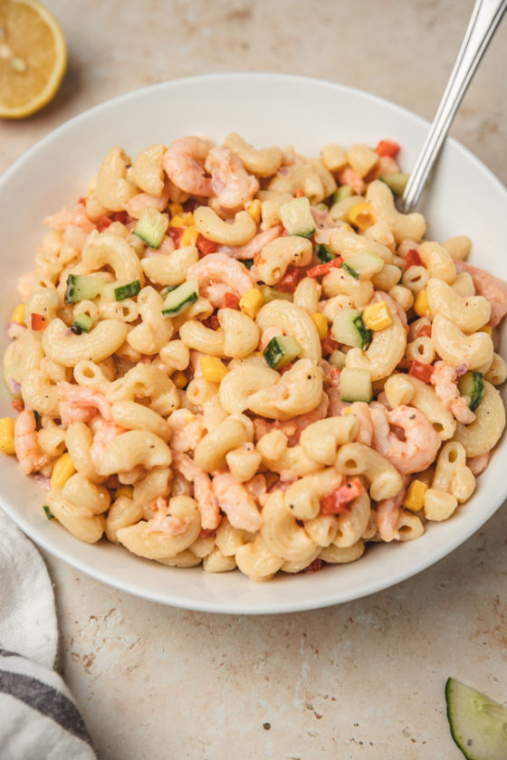 pasta salad in a white bowl with a spoon placed beside a white and grey napkin.