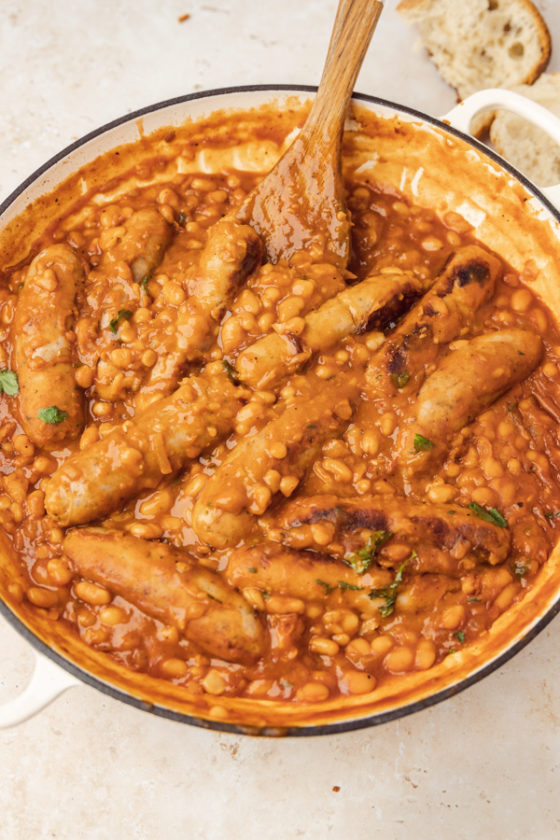 a casserole pan of baked beans casserole with a ustic bread on the side of the pan.