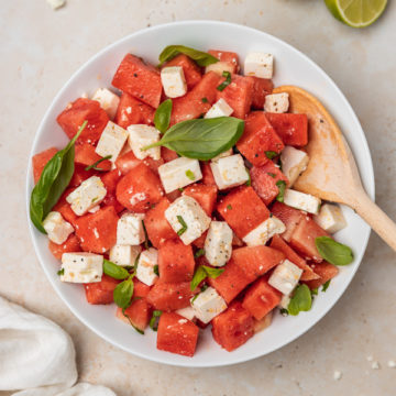 a bowl of watermelon feta salad with fresh basil and a wooden serving spoon.