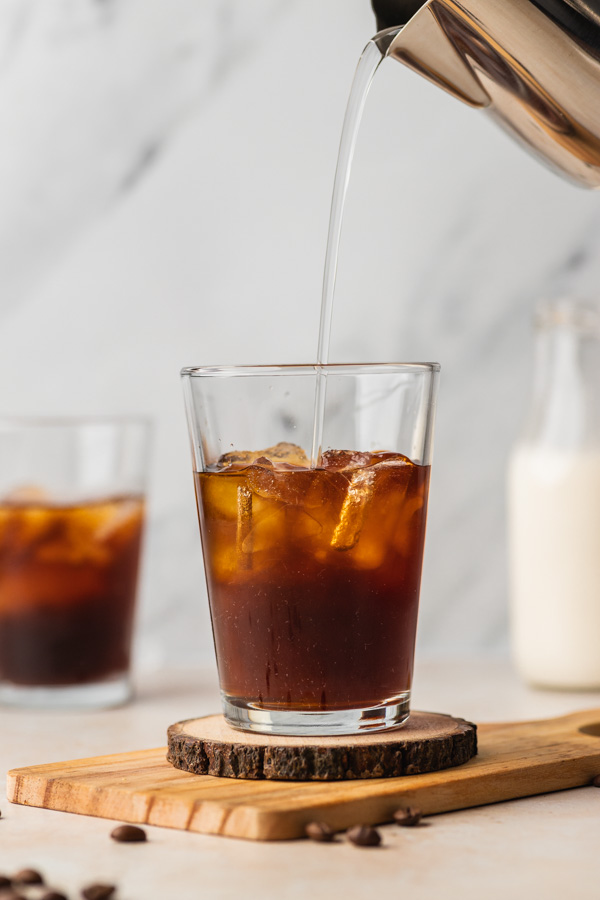 a hand pouring water over iced cold brew.