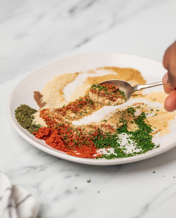 a hand mixing spices on a small plate.
