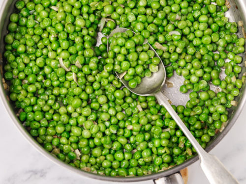 sauteed garden peas in a skillet with serving spoon.