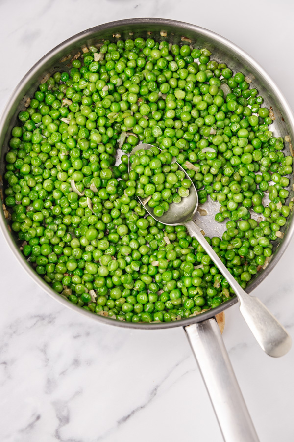 sauteed garden peas in a skillet with serving spoon.