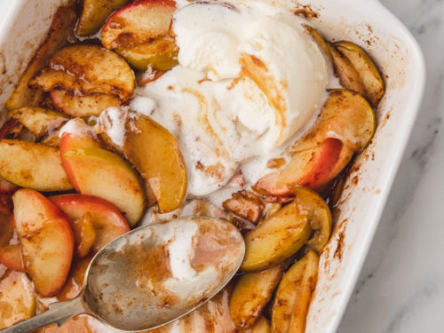 baked apple slices in a baking dish topped with ice cream.