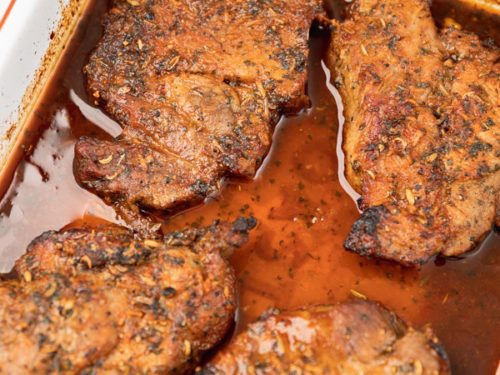 four cooked steaks in a baking sheet sitting in the delicious marinade juice.