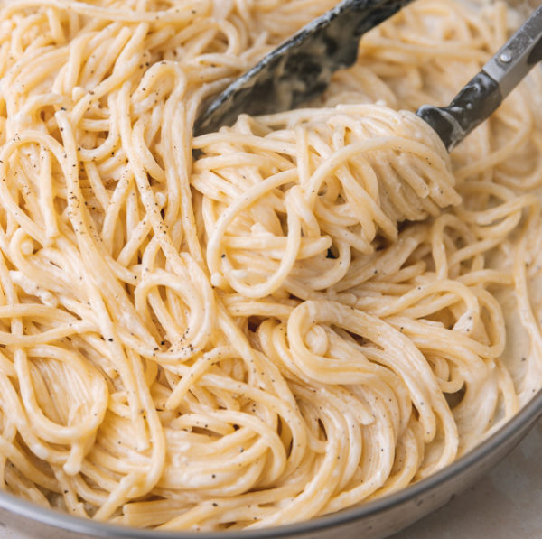 a close up of creamy spaghetti pushed in a skillet with a kitchen tong.