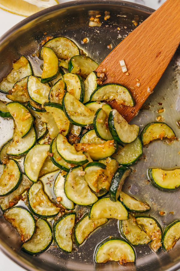 sauteed garlic butter zucchini in a skillet with a wooden ladle pushing into it.