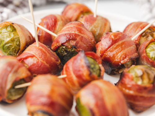a platter of bacon wrapped brussel sprouts on a toothpick.
