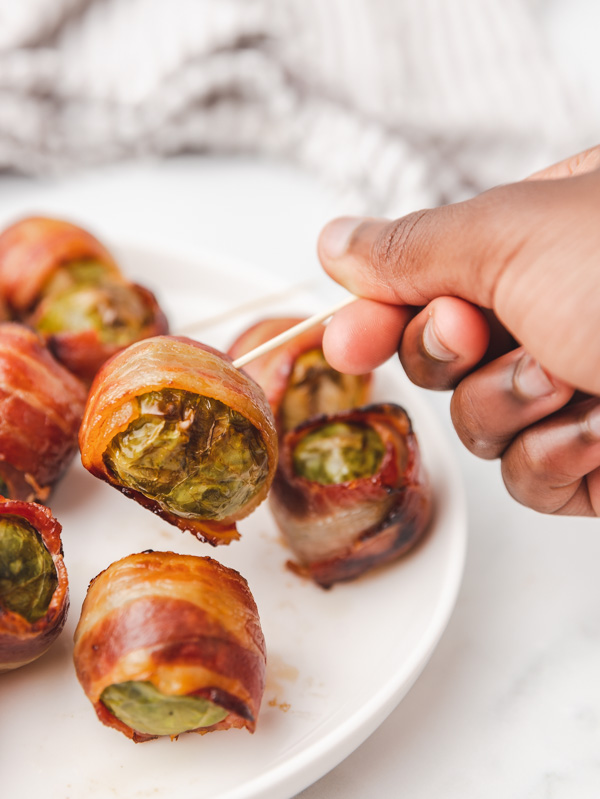 a hand holding up bacon wrapped vegetable on a toothpick.