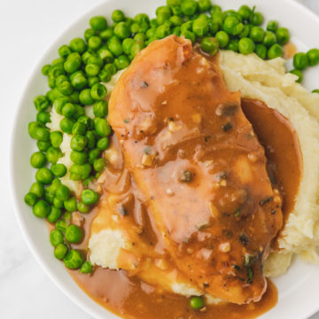 a plate of chicken breast gravy served over mashed potatoes and peas.