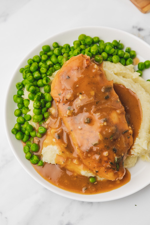 a plate of mashed potatoes and chicken gravy with green peas.