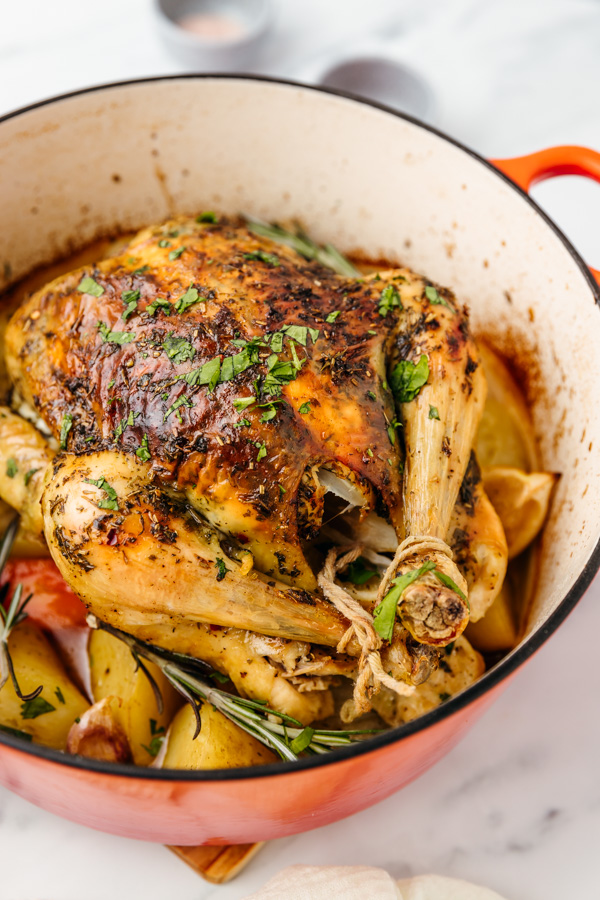 roasted whole chicken sitting on a bed of potatoes in a dutch oven.