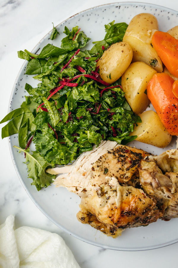 a large plate of cooked potatoes, carrots, green salad and chicken.