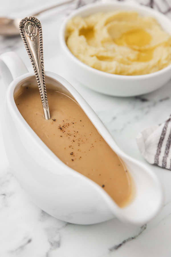 a spoon inderted in a gravy boat placed beside a bowl of mashed potatoes.