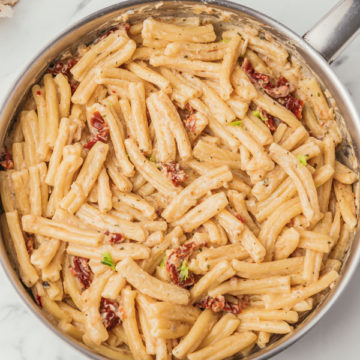 creamy pasta with specks of sundried tomatoes in a skillet.