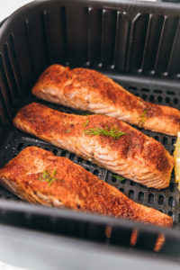 3 salmon fillets with lemon slices in an air fryer basket.