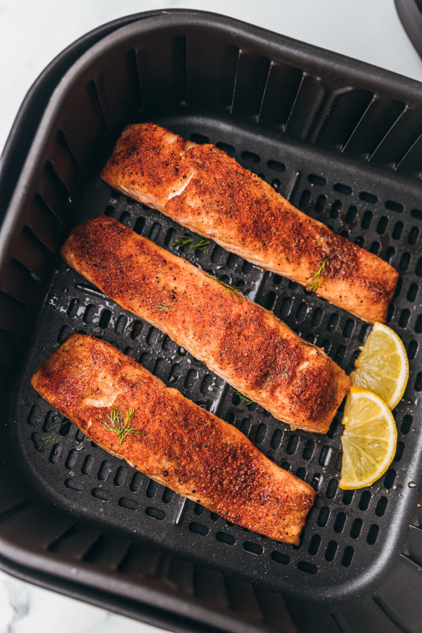 three coked salmon fillets in air fryer basket.