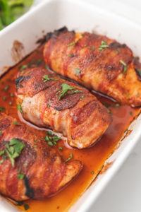 three cooked bacon wrapped chicken breast in a baking dish.