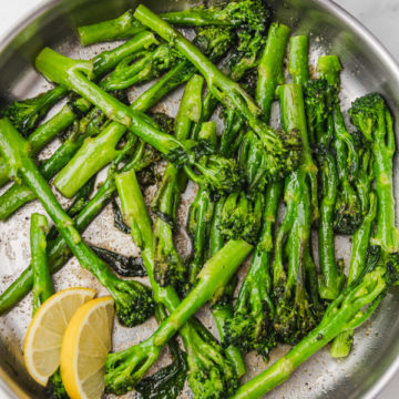 sauteed broccolini with lemon wedges in a skillet.