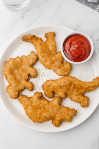 four dino nuggets on a white plate with ketchup.