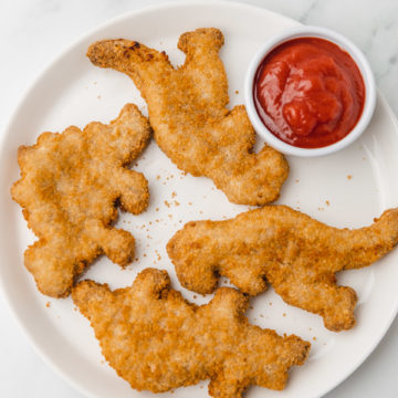 four dino nuggets on a white plate with ketchup.