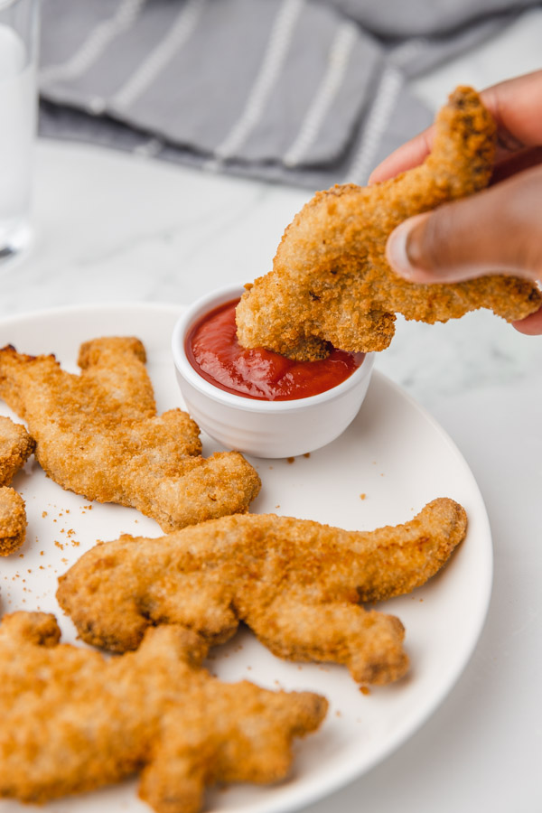 a hand dipping nugget in a pot of ketchup.