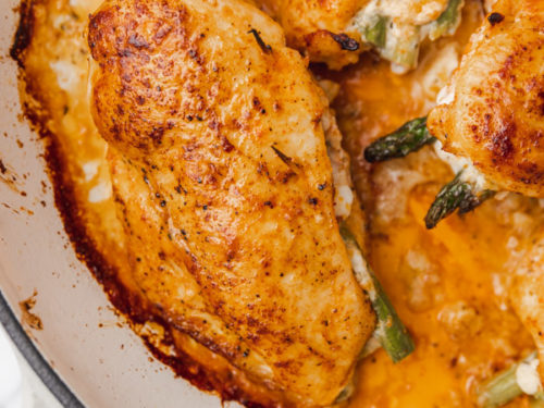 a close up on asparagus stuffed chicken in a cast iron.
